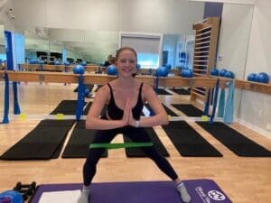 lady with her hands together standing on the mad with the resistance band connecting her legs in the fitness studo